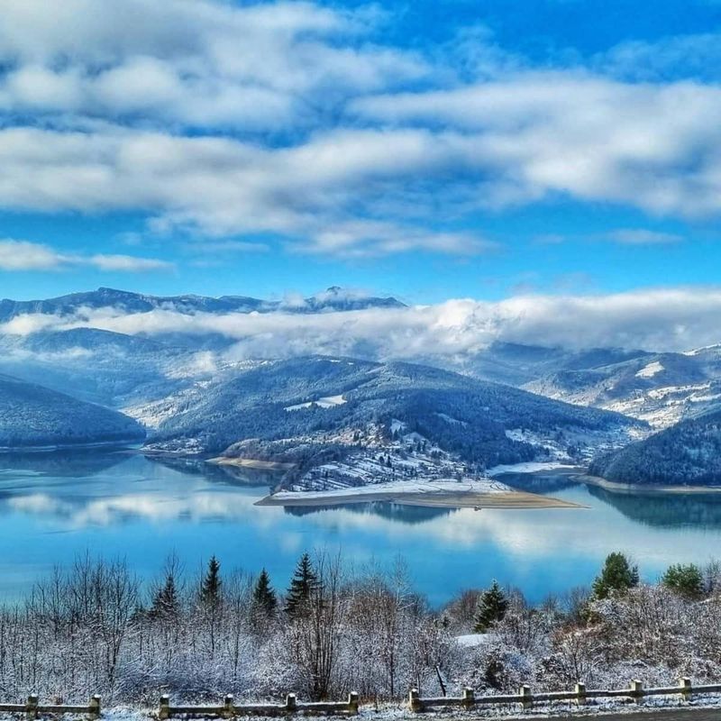 Lacul Izvorul Muntelui iarna, cu munți înzăpeziți și nori